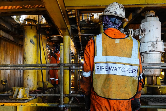 fire watcher oversees a welder on an oil rig